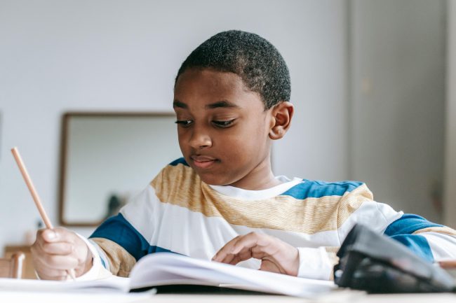 Petit garçon métisse qui écrit sur un cahier