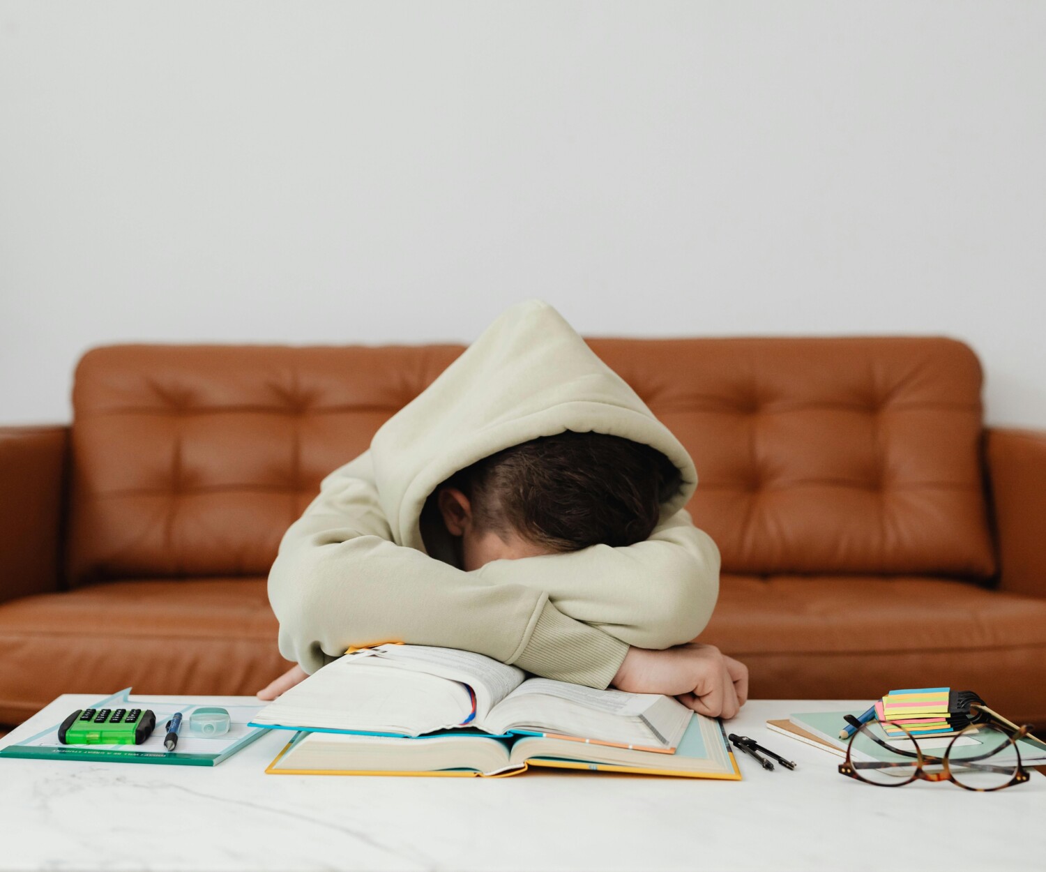 Enfant qui boude devant ses devoirs. Il a une capuche sur la tête.